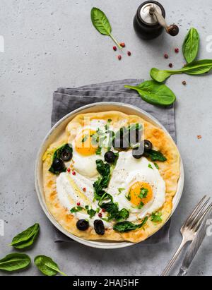 Türkische Eier Fladenbrot mit Joghurt, Käse, Oliven, Spinat und rotem Pfeffer auf Keramik-Vintage-Teller auf grauem altem Hintergrund. Draufsicht. Stockfoto