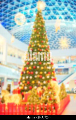 Ein unschärfes Bild eines hohen, verkleideten Weihnachtsbaums in der Lobby eines Einkaufszentrums. Atmosphäre vor dem Urlaub. Stockfoto