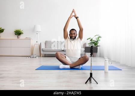 Serious ruhigen jungen afroamerikanischen Mann mit Bart, weiße Sportbekleidung in Lotus Position nimmt Video auf Handy Webcam Stockfoto