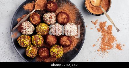 Vielfalt an hausgemachten dunklen Schokoladentrüffeln mit Kakaopulver, Pistazien, Mandeln in hellgrauer Hintergrundtextur. Draufsicht, Kopierbereich. Stockfoto