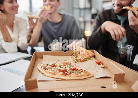 Nahaufnahme einer frischen Pizza in der geöffneten Box mit Geschäftsleuten, die im Hintergrund am Tisch zu Mittag essen Stockfoto