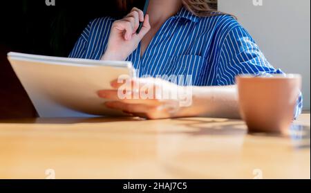 Frauen halten den Notizblock in der Nahaufnahme, lesen den Lehrplan im Café mit einer Kaffeetasse auf einem Holztisch. Platz für Text kopieren, der verfügbar ist. Stockfoto