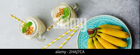 Bananenmoothie mit Müsli, getrockneten Früchten und Minze auf grauem Betongrund. Draufsicht. Stockfoto