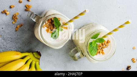 Bananenmoothie mit Müsli, getrockneten Früchten und Minze auf grauem Betongrund. Draufsicht. Stockfoto