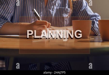 Planungskonzept. Notizen schreiben, Pläne in Notizbuch auf Holztisch mit Kaffeetasse. Stockfoto