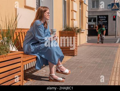 Junge, moderne Frau, die im Sommer mit einer wiederverwendbaren Öko-Kaffeetasse im Freien ausruht und den Lebensstil der Stadt genießt. Stockfoto