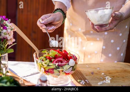 Gemüsesalat mit Mozzarella-Käse. Frau, die im Freien auf dem Tisch mediterrane Speisen zubereitete Stockfoto