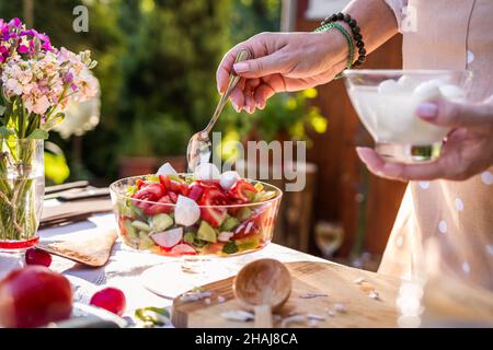 Gemüsesalat mit Mozzarella-Käse. Frau, die im Freien auf dem Tisch mediterrane Speisen zubereitete Stockfoto