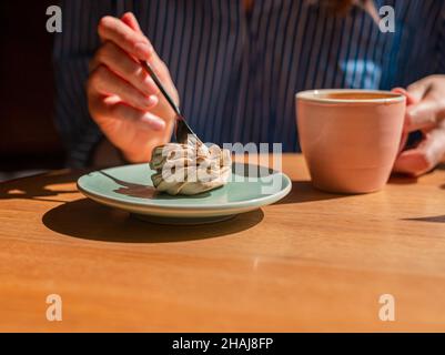 Frauen Hand Nahaufnahme und Kaffeetasse und süße Dessert zefir und medizinische Gesichtsmaske auf Holzschreibtisch im Café. Stockfoto