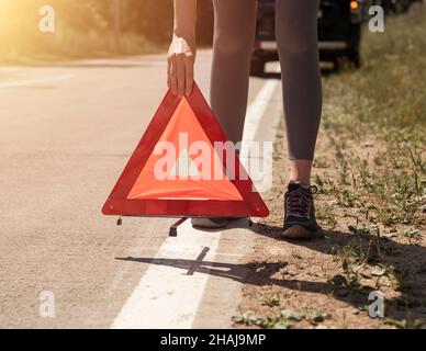 Junge Frauen stellen sich die Hände aus der Nähe, indem sie ein Warnschild auf der Straße in der Nähe eines kaputten Autos am Straßenrand angebracht haben. Stockfoto