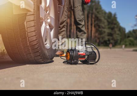 Tragbare Reifenpumpe zum Aufpumpen des Autorads, Ansicht von unten. Reifenaufblasvorrichtung mit Manometer in Nahaufnahme der Straße. Stockfoto