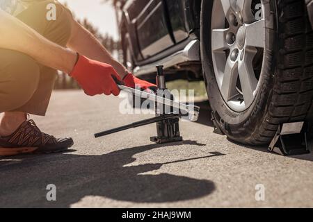 Hydraulischer Wagenheber wird unter Auto von den Händen in den Handschuhen, Nahaufnahme gesetzt. Stockfoto