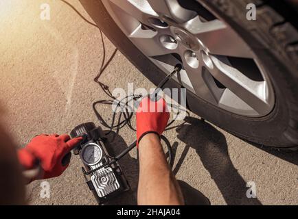 Reifenpumpe, die das Autorad aufpumpt. Reifenaufblasvorrichtung in männlichen Händen, Draufsicht. Stockfoto