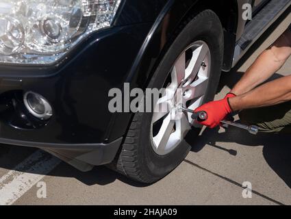 Männliche Hände Befestigung und Überprüfung Radreifen des modernen schwarzen Autos mit manuellem Metallwerkzeug, Nahaufnahme. Stockfoto