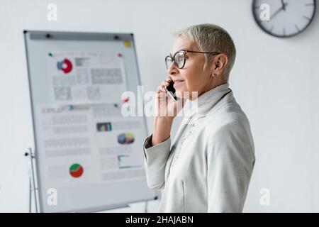 Lächelnde Geschäftsfrau mit grauem Haar, die im Büro auf dem Mobiltelefon spricht Stockfoto