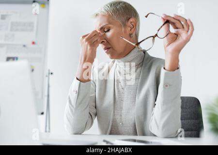 Müde Geschäftsfrau mit grauen Haaren, die die Augen berühren und eine Brille halten Stockfoto