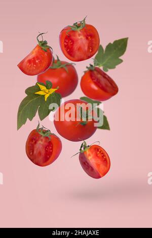 In Scheiben geschnittene und ganze Tomaten fliegen in der Luft, isoliert auf hellrosa Hintergrund. RAW vegetarische gesunde Ernährung Zutat. Kreatives Food-Konzept. Stockfoto