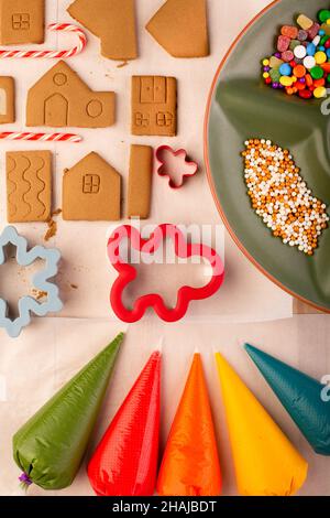 Lebkuchenhauskekse, die bereit sind, mit farbiger königlicher Glasur dekoriert zu werden. Traditionelles weihnachtshandwerk für die Familie. Stockfoto