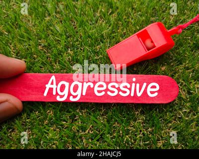 Hand halten farbigen Eis Stick mit Text aggressiv auf einem grünen Gras Hintergrund geschrieben Stockfoto