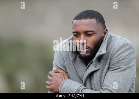 Gestresster Mann mit schwarzer Haut, der im Winter mit einer Jacke im Freien erkältet wird Stockfoto