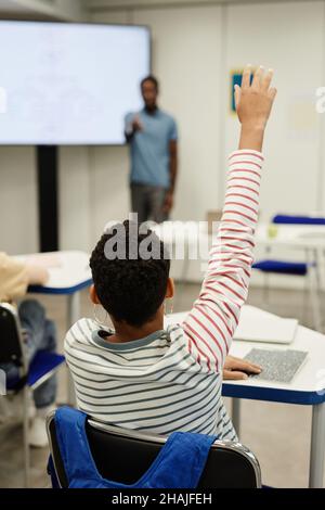 Vertikale Rückansicht Porträt eines afroamerikanischen Jungen, der in der Klasse die Hand hebt Stockfoto