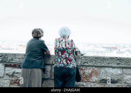 Budapest, Ungarn, 19. September 2019: Rückansicht von zwei älteren Frauen, die vom Balkon aus auf die Altstadt blicken und auf der Stadtstraße spazieren gehen. Touristen, die in E reisen Stockfoto