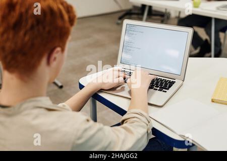 Porträt eines rothaarigen Jungen im Teenageralter, der einen Laptop benutzt, während er im Klassenzimmer codiert und Platz kopiert Stockfoto