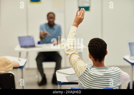 Rückansicht Porträt eines afroamerikanischen Teenagers, der im Klassenzimmer die Hand hebt und den Raum kopiert Stockfoto