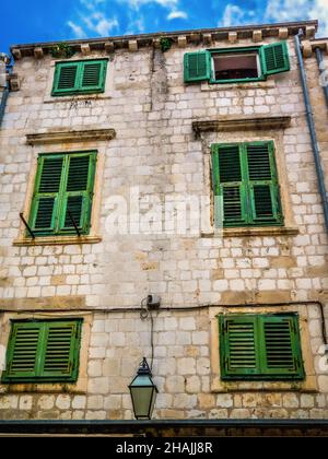 Blick auf ein klassisches hohes Gebäude mit grünen Fensterläden, die in den strahlenden mediterranen Sonnenschein getaucht sind, aufgenommen in Dubrovnik, Kroatien am 9th. Juni 2013 Stockfoto