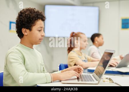 Seitenansicht Porträt eines Jungen im Teenageralter, der einen Laptop in der Codierungsklasse für Kinder verwendet, Kopierbereich Stockfoto