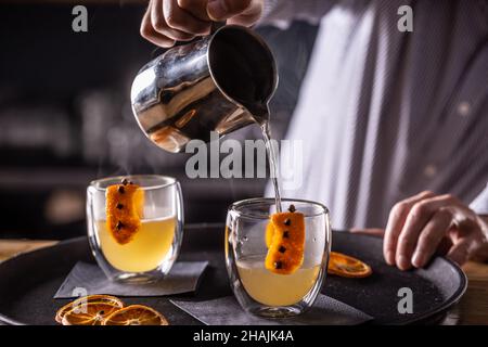 Der Barkeeper im Pub oder Restaurant bereitet das HEISSE WINTERGETRÄNK zu und gießt es in Glassbecher. Stockfoto