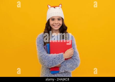 Glückliches Kind in Pullover und Hut halten Arbeitsbuch auf gelbem Hintergrund, Bildung Stockfoto