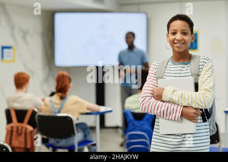 Waist-up-Porträt eines lächelnden Teenagers, das Bücher hält und die Kamera im Klassenzimmer anschaut, Platz zum Kopieren Stockfoto