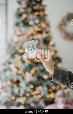 Nahaufnahme der Hand der Frau, die das Bild des geschmückten Weihnachtsbaums hält. Stockfoto