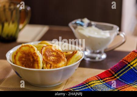 Hausgemachte russische Pfannkuchen auf einer Keramikschüssel auf dem Esstisch - Nahaufnahme mit selektivem Fokus und einer Soßenschüssel mit saurer Creme vor verschwommenem Hintergrund Stockfoto