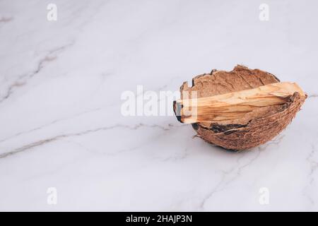 Brennender Palo Santo Baum klebt in der Kokosnussschale auf hellem Marmortischhintergrund - heiliger Weihrauchbaum aus Lateinamerika. Meditation, geistige Gesundheit Stockfoto