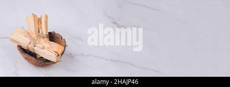 Banner mit Palo Santo Baumstäben in Kokosnussschale auf hellem Marmortisch Hintergrund - heiliger Weihrauchbaum aus Lateinamerika. Meditation, geistige er Stockfoto