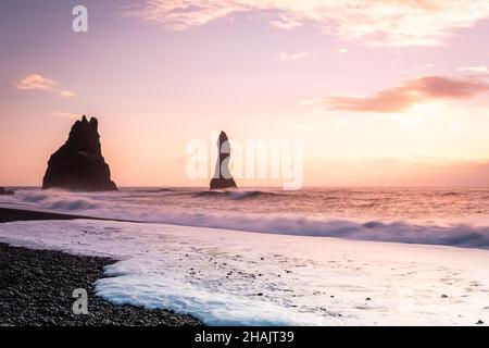 Rund um Vik, Island, schwarze Sandstrände Sonnenschein Tag wunderschöne goldene Lichtklippen Schnee und Eisstapel im Meer Stockfoto