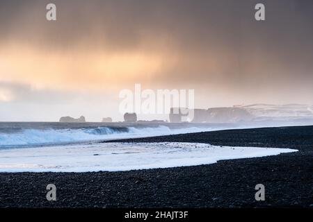 Rund um Vik, Island, schwarze Sandstrände Sonnenschein Tag wunderschöne goldene Lichtklippen Schnee und Eisstapel im Meer Stockfoto