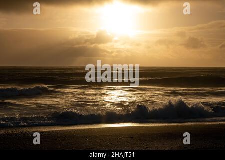 Rund um Vik, Island, schwarze Sandstrände Sonnenschein Tag wunderschöne goldene Lichtklippen Schnee und Eisstapel im Meer Stockfoto