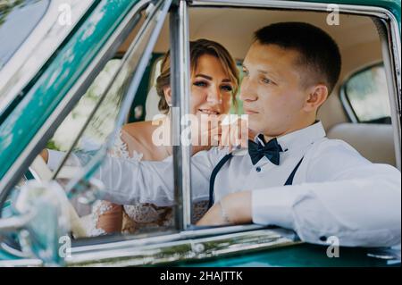 Wunderschöne stilvolle blonde Braut posiert im Retro-grünen Auto mit Bräutigam. Braut und Bräutigam sitzen im Retro-Auto. Hochzeit, Braut und Bräutigam Stockfoto