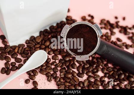 Makro-Nahaufnahme der weißen Folie Kaffeebohne Beutel Mock up mit Kaffeebohnen und Portafilter auf hellrosa Hintergrund Stockfoto