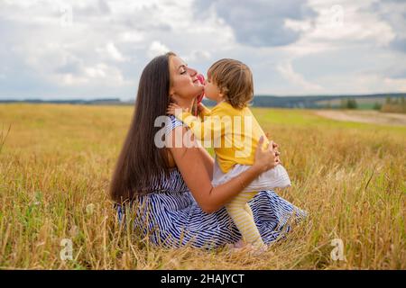 Kleines Mädchen in einem Kleid und einer Brille küsst ihre Mutter auf einem Sommerfeld Stockfoto