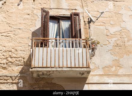 Alter Balkon mit alten hölzernen Fensterläden an der Steinmauer des typischen alten mediterranen Hauses in Sizilien. Stockfoto