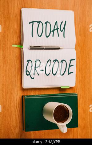 Schild mit QR-Code. Wort für die Marke für eine Art von Matrix-Barcode Ein maschinenlesbarer Code Plain Blank Notebooks und Ein Stift neben Einer Tasse Stockfoto