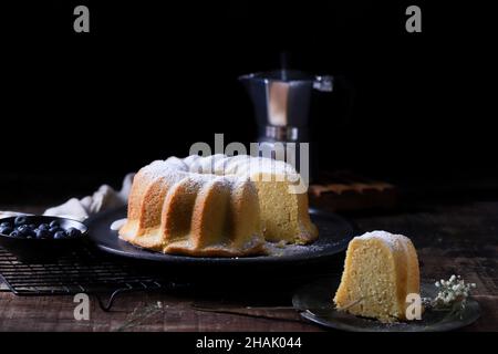Hausgemachter Kuchen in Scheiben mit Heidelbeeren auf der Seite und eine Kaffeemaschine im Hintergrund Stockfoto