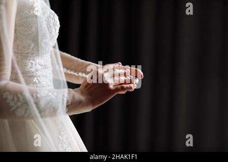 Zugeschnittenes Foto von sanften Händen der Braut, die in einem weißen Spitzenkleid steht, legt einen Ehering auf ihren Finger. Hochzeitstag. Platz für Text. Stockfoto