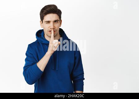 Schöner kokett Kerl winken, zeigt Stille, shush nicht sprechen Geste und winken, hat Geheimnis, sein ruhiges Zeichen, stehen über weißem Hintergrund Stockfoto
