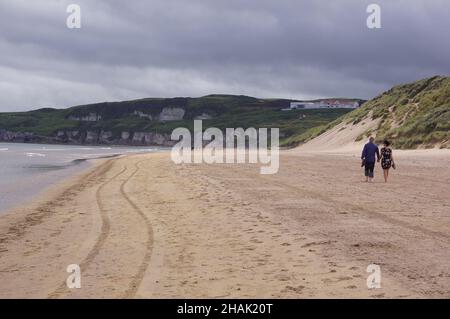 Ein Paar, das an der Küste von Whiterocks Beach in Portrush, Grafschaft Antrim, Nordirland, entlang geht Stockfoto