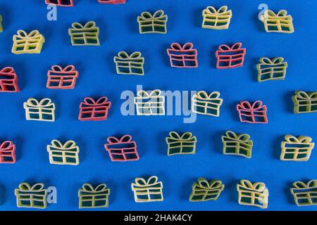 Kreativer Hintergrund für den Urlaub. Rohe Pasta in Form von Weihnachtsgeschenk in grünen, roten und gelben Farben auf blauem Hintergrund. Nahaufnahme. Flach liegend. Stockfoto